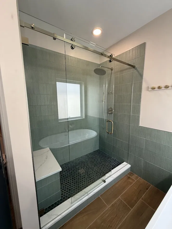 Custom tiled shower with sage green tile, hex floor, and sliding glass door by CNB Renovations